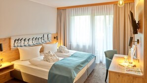 Habitación de hotel con una cama grande, un escritorio con silla, un cuadro en la pared y una ventana con cortinas.