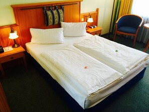 A hotel room with a double bed, two bedside tables with lamps, a chair, and a wooden headboard. - Erlebnis Hotel Chiemgauer Hof (Inzell)