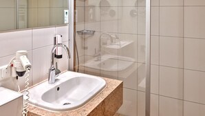 Un baño moderno con ducha de vidrio, lavamanos con encimera de granito y espejo sobre él.
