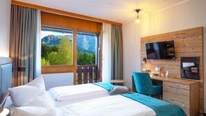 A hotel room with a bed, a desk, a chair, a TV, and a view of mountains. - Erlebnis Hotel Chiemgauer Hof (Inzell)