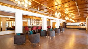 Un vestíbulo espacioso con techo de madera, mostrador de recepción y una zona de bar con taburetes rojos.