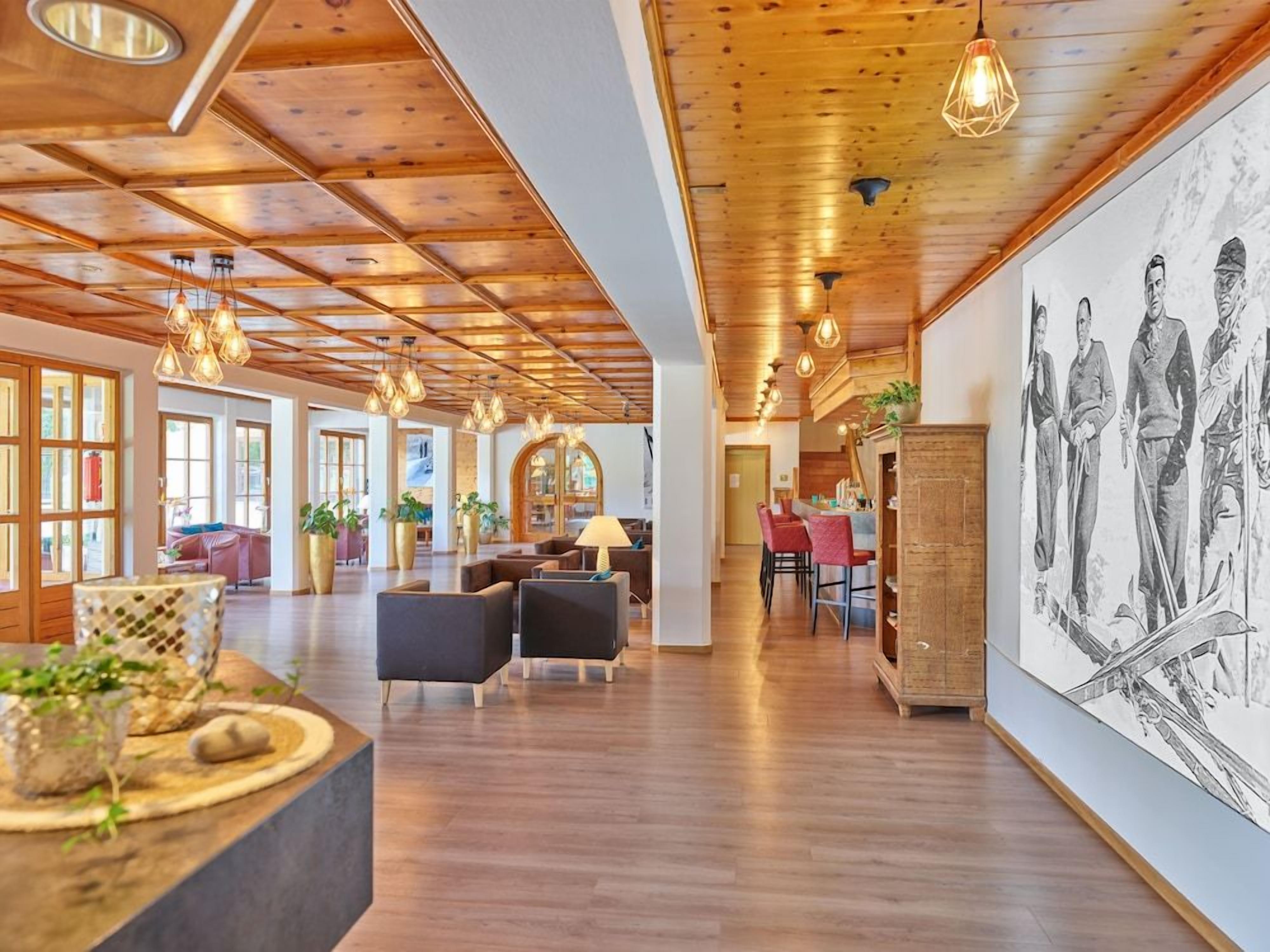 Eine geräumige Lobby mit Holzbalkendecke, Pendelleuchten und einem großen Wandgemälde.