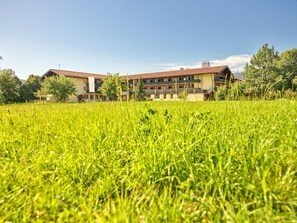 A hotel with a large outdoor grassy area in front, multiple floors, and a red roof. - Erlebnis Hotel Chiemgauer Hof (Inzell)