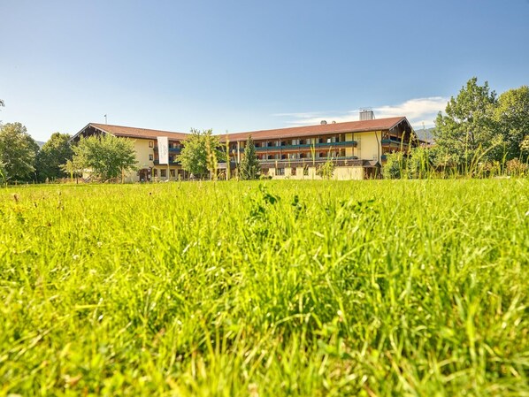 A hotel with a large outdoor grassy area in front, multiple floors, and a red roof. - Erlebnis Hotel Chiemgauer Hof (Inzell)