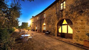 A stone building with a courtyard, outdoor seating, and a large arched window. - Sarna Residence (San Quirico d'Orcia)