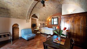 Una habitación acogedora con techo de ladrillo, una cama, un sofá azul con estampado, una mesa de madera con un jarrón de flores y un armario de madera.