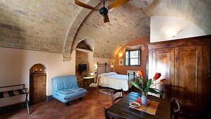 A cozy room with a brick ceiling, a bed, a blue patterned sofa, a wooden table with a vase of flowers, and a wooden cabinet. - Sarna Residence (San Quirico d'Orcia)