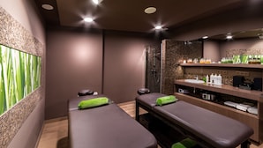 Une salle de spa équipée de deux tables de massage, d’un espace douche et d’étagères contenant des produits de toilette.