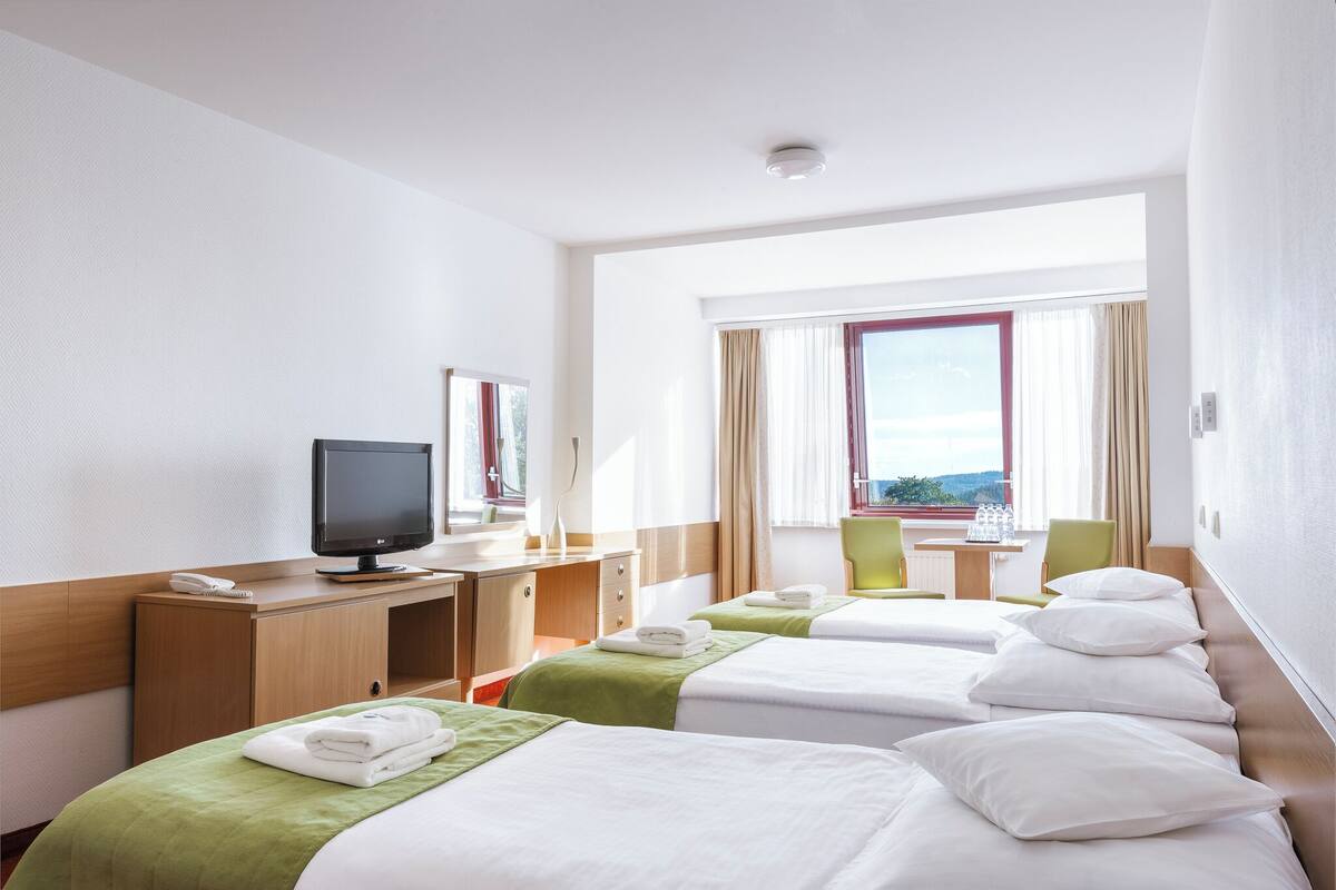 Habitación de hotel con dos camas, un escritorio con computadora, televisor y ventana con cortinas.