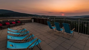 Une terrasse avec des chaises et une table, offrant une vue imprenable sur un paysage magnifique au coucher du soleil.