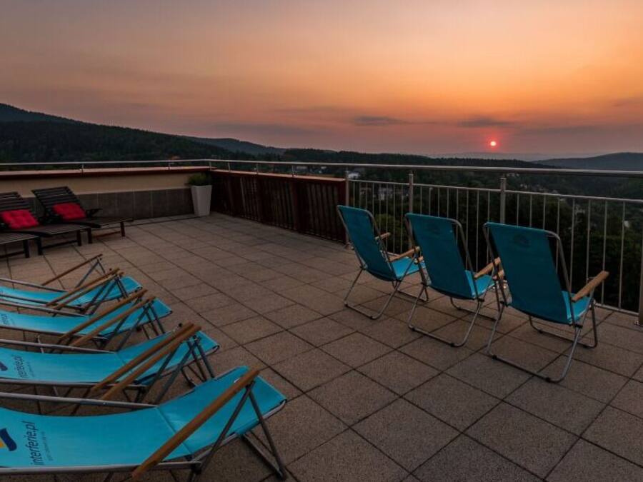 A terrace with chairs and a table, overlooking a scenic landscape during sunset.