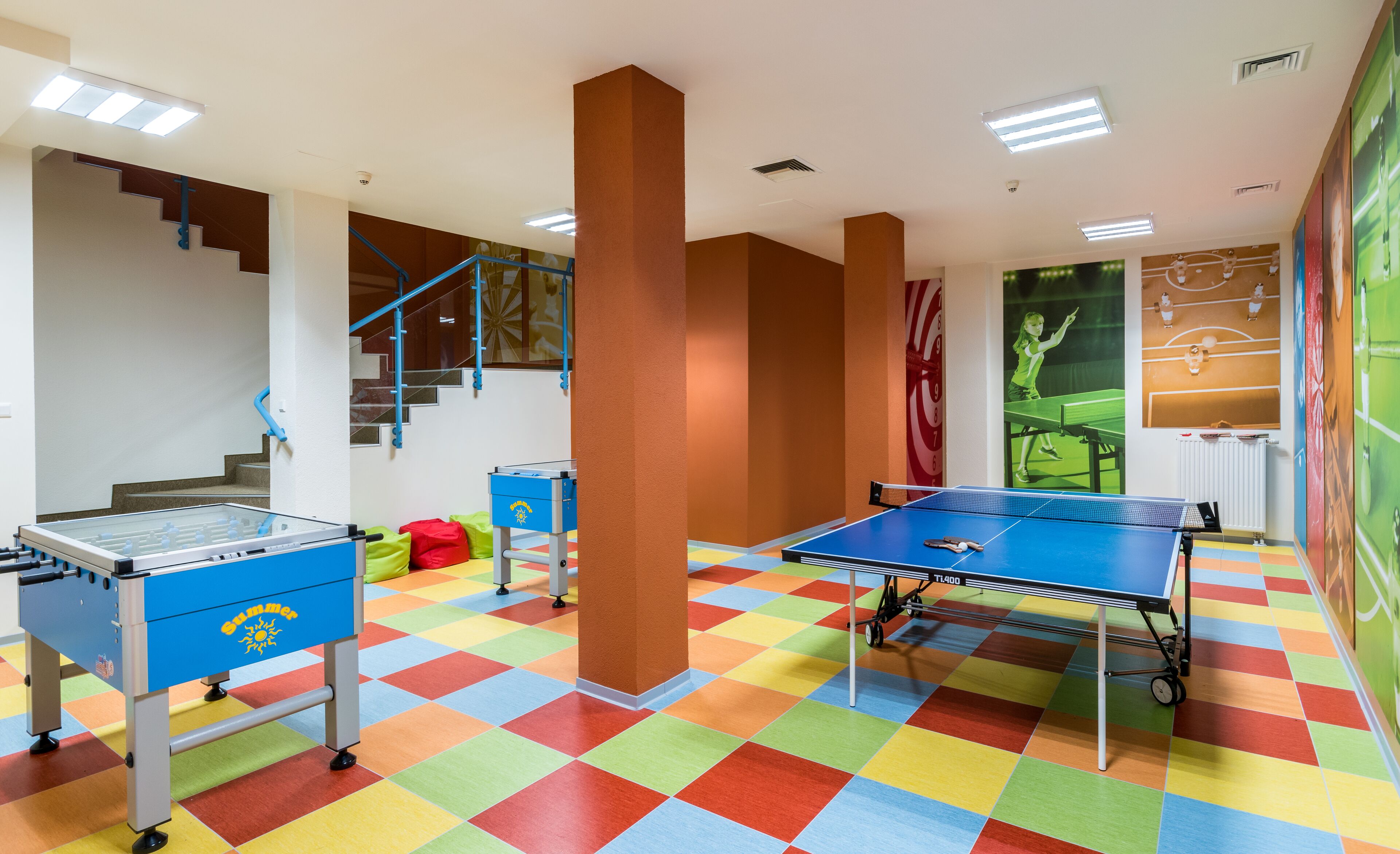 Een kamer met een tafelvoetbaltafel, een pingpongtafel en een trap.