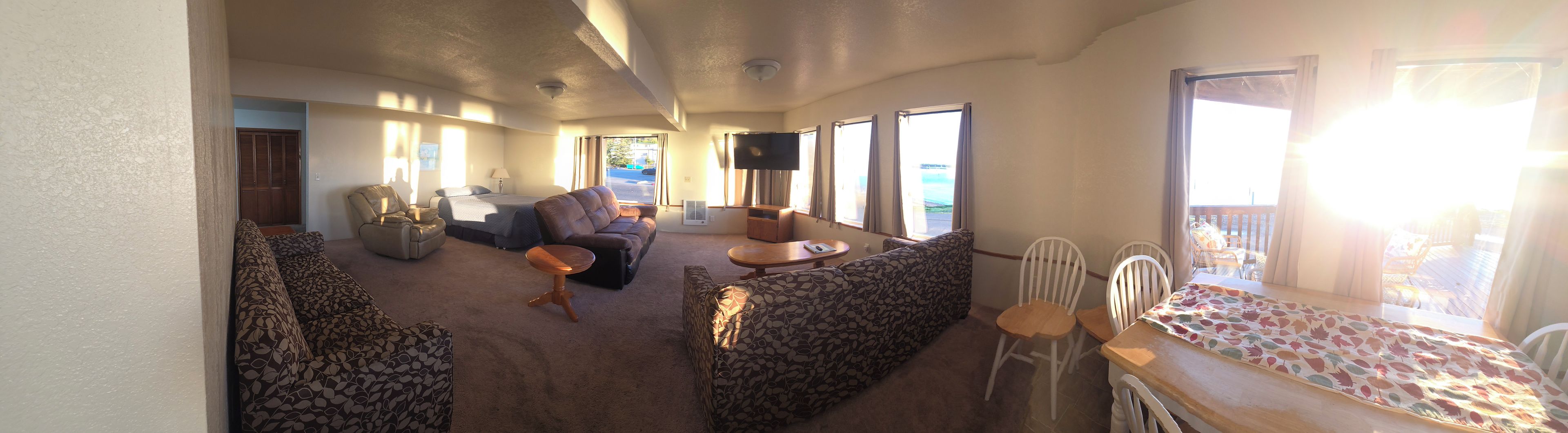 A living room with a sofa, armchair, and a small table. There is a TV mounted on the wall and a window with curtains.