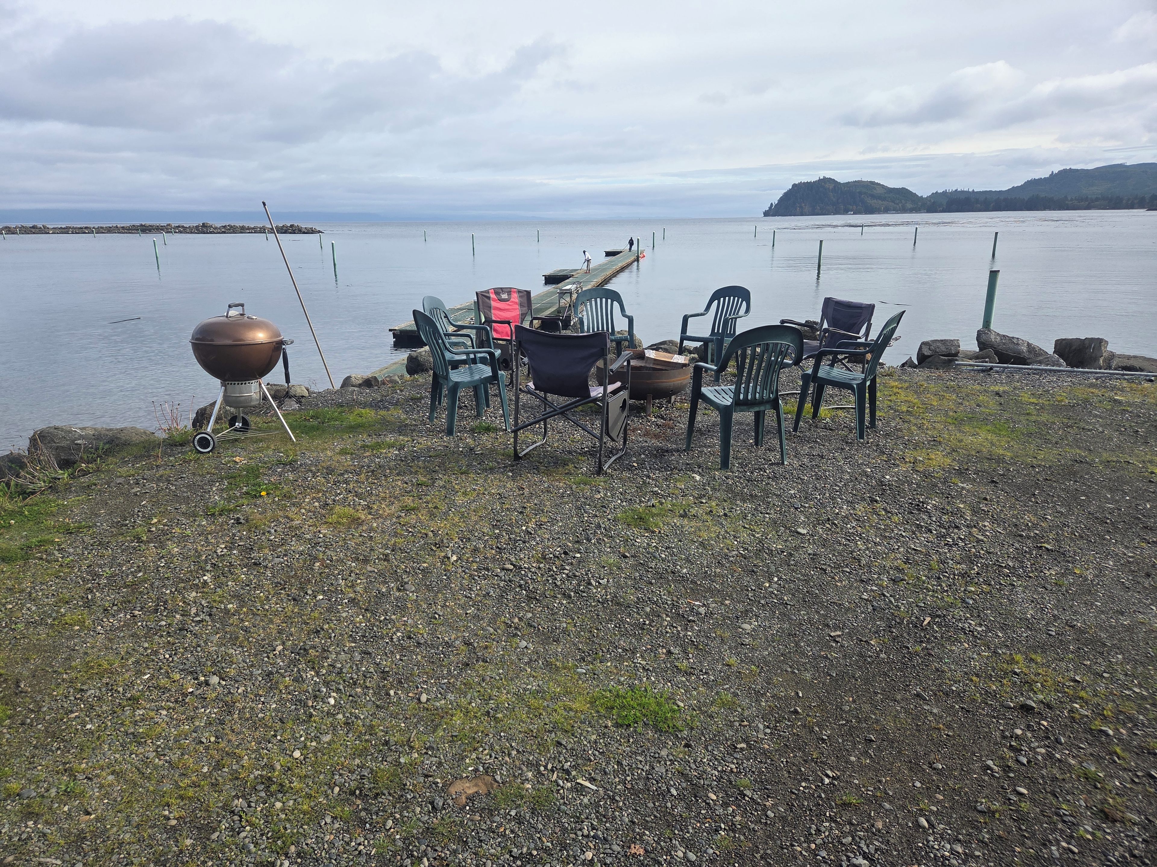 A lakeside setting with a barbecue grill, chairs, and a view of the water.