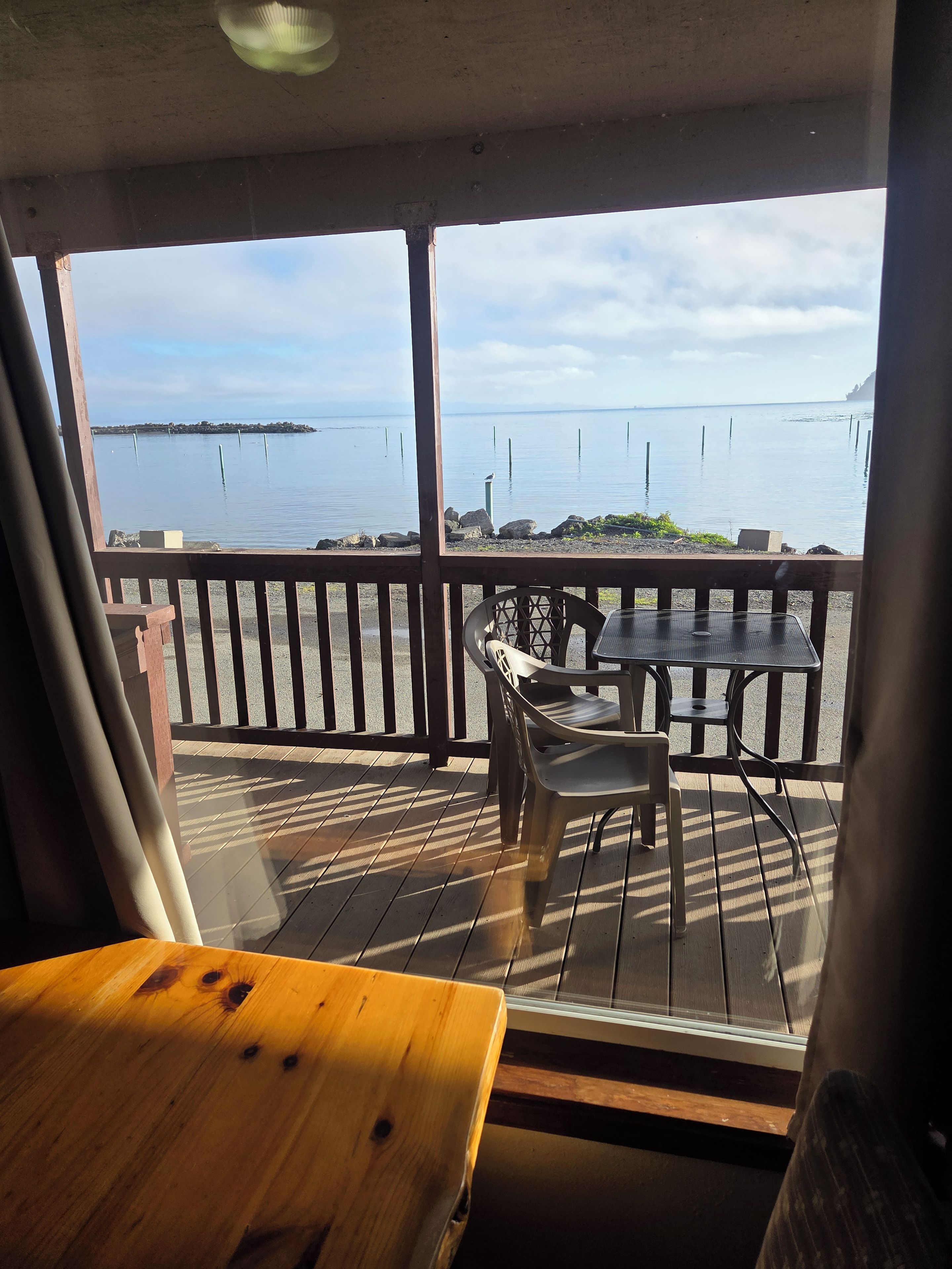 Una terraza de madera con una mesa y sillas, con vista a una masa de agua tranquila y una costa lejana.