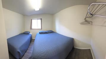 A room with two beds, a window, and a metal rack.