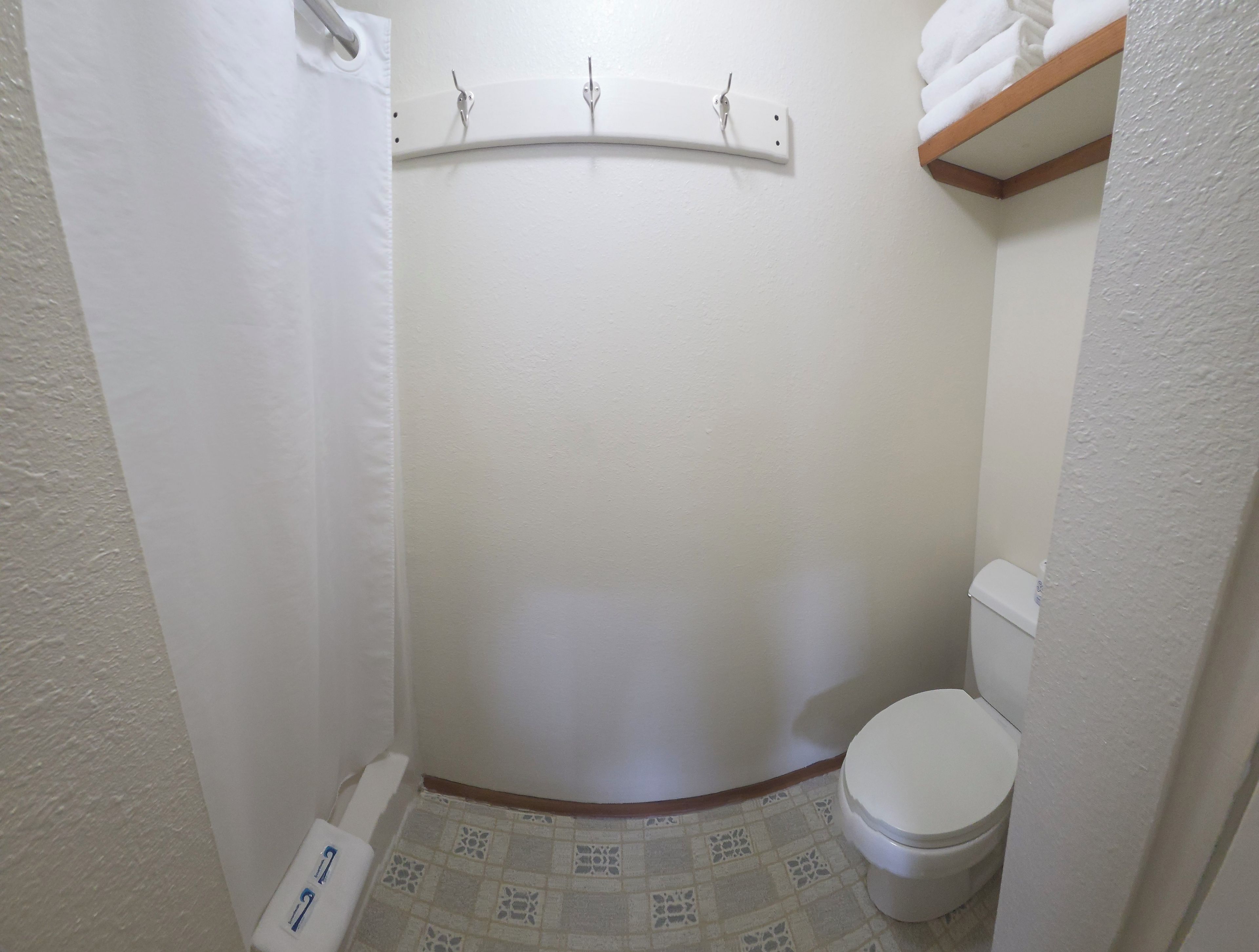 A small, white bathroom with a toilet, a shower stall, and a towel rack.