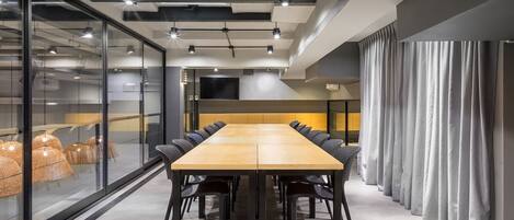 A conference room with a long table, black chairs, and glass walls.