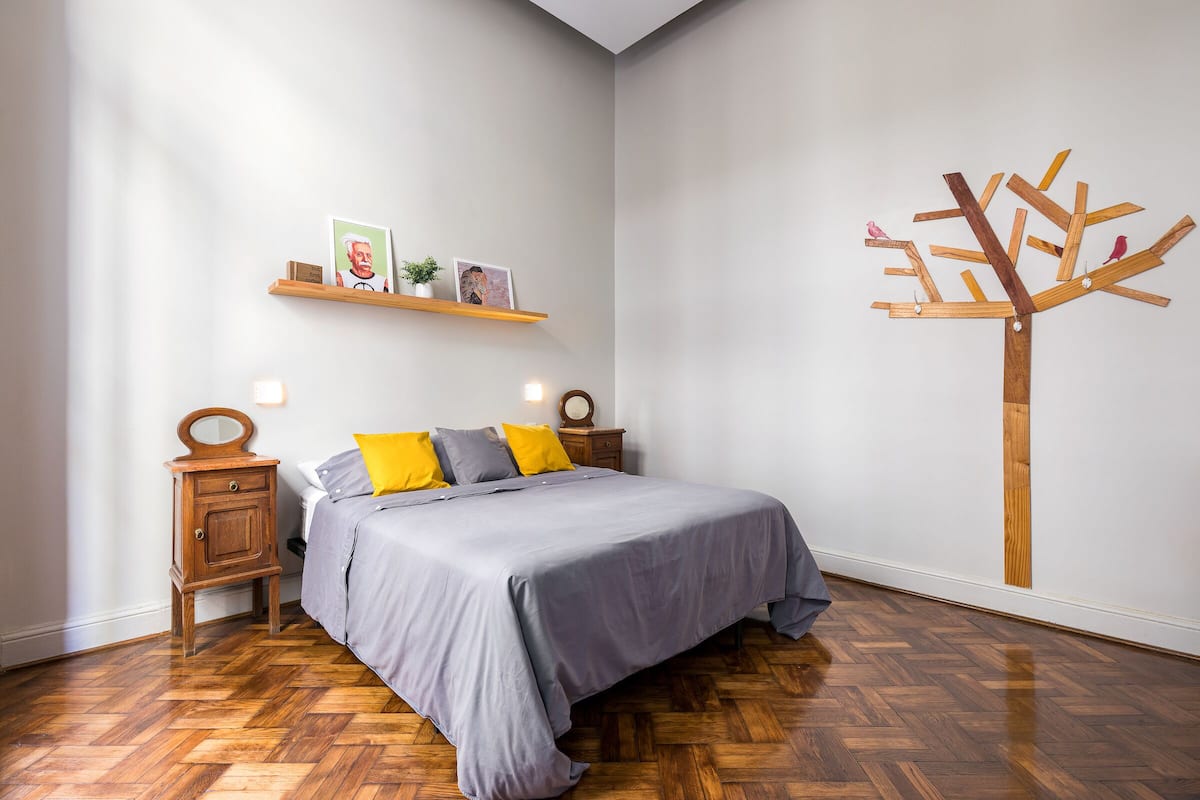 Un dormitorio con cama, mesitas de noche de madera, un estante con fotografías y un cuadro de un árbol.