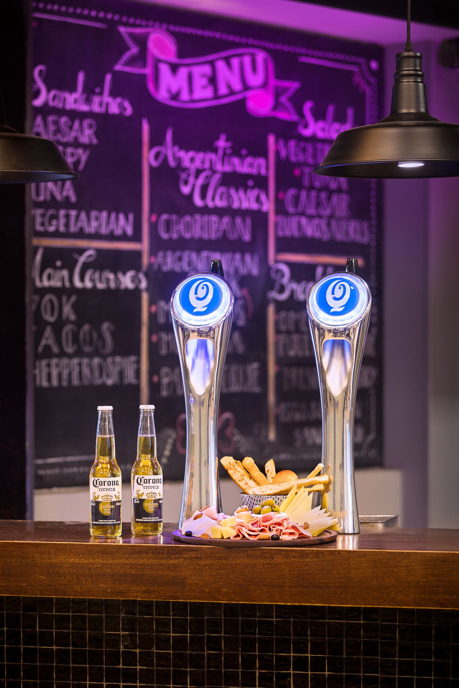 A bar counter with two Corona beer bottles, a tap, and a selection of snacks.