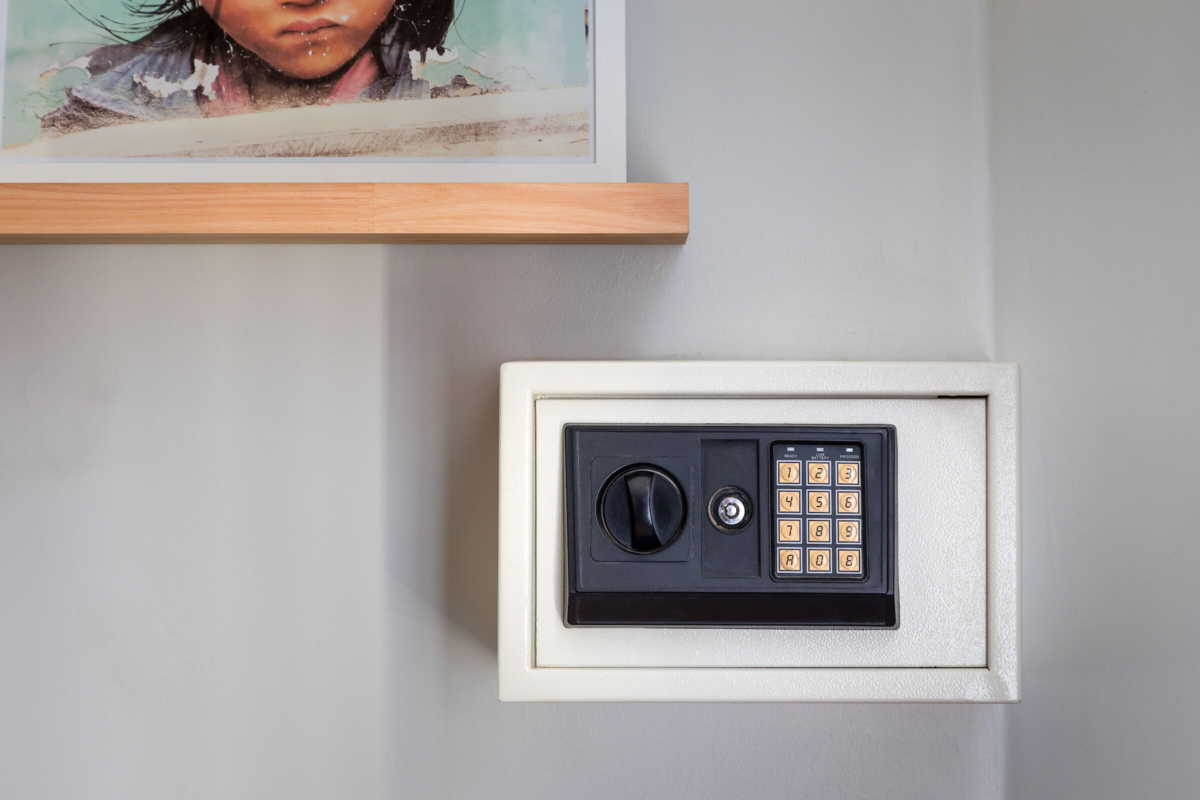 A wall-mounted safe with a numeric keypad and a keyhole, and a framed artwork above it.
