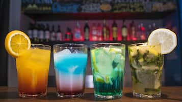 Cuatro vasos de cócteles coloridos con hielo, adornados con rodajas de cítricos, sobre una barra.