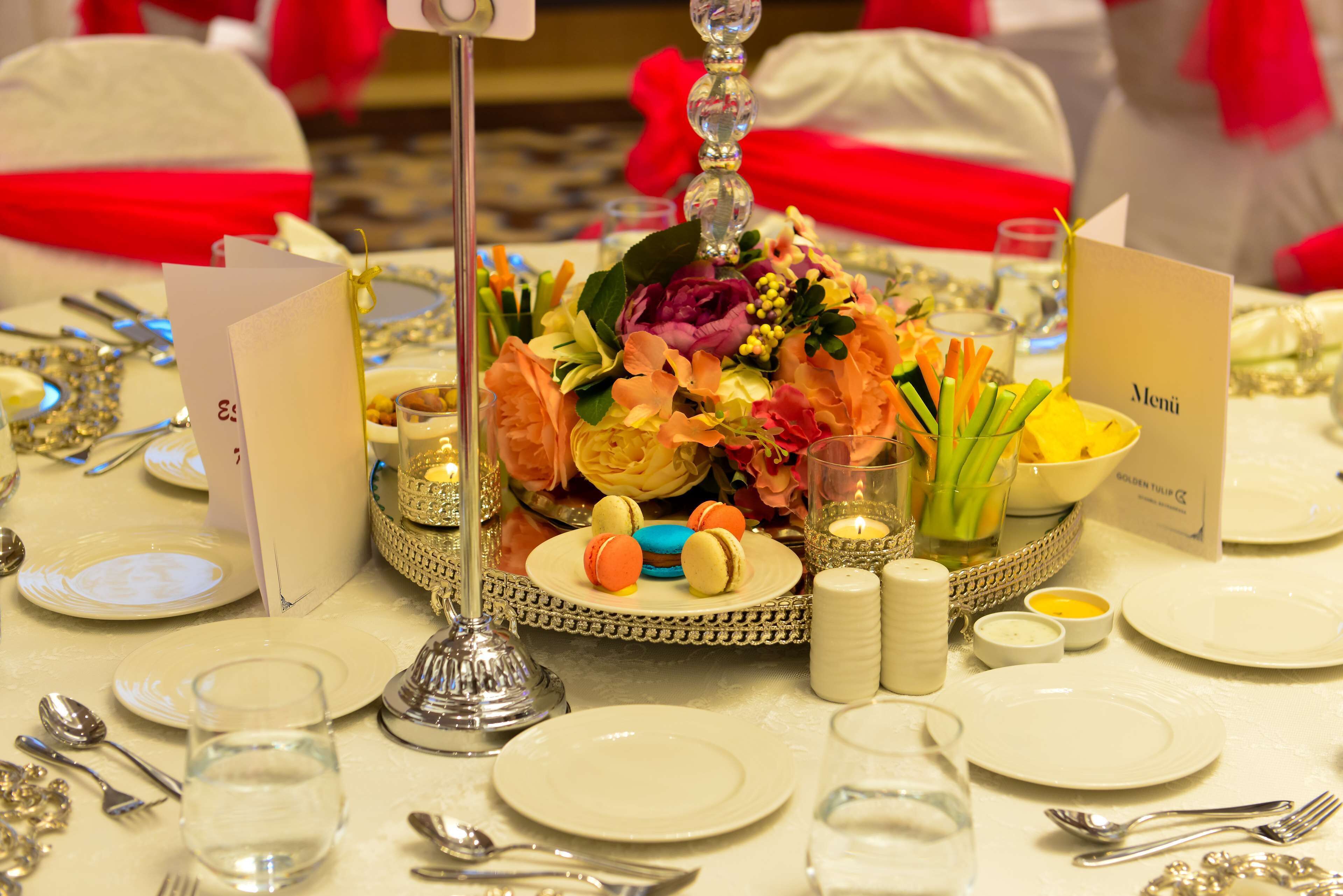 Uma mesa posta para um evento formal, com um arranjo central, cartões de menu e diversos utensílios de mesa.