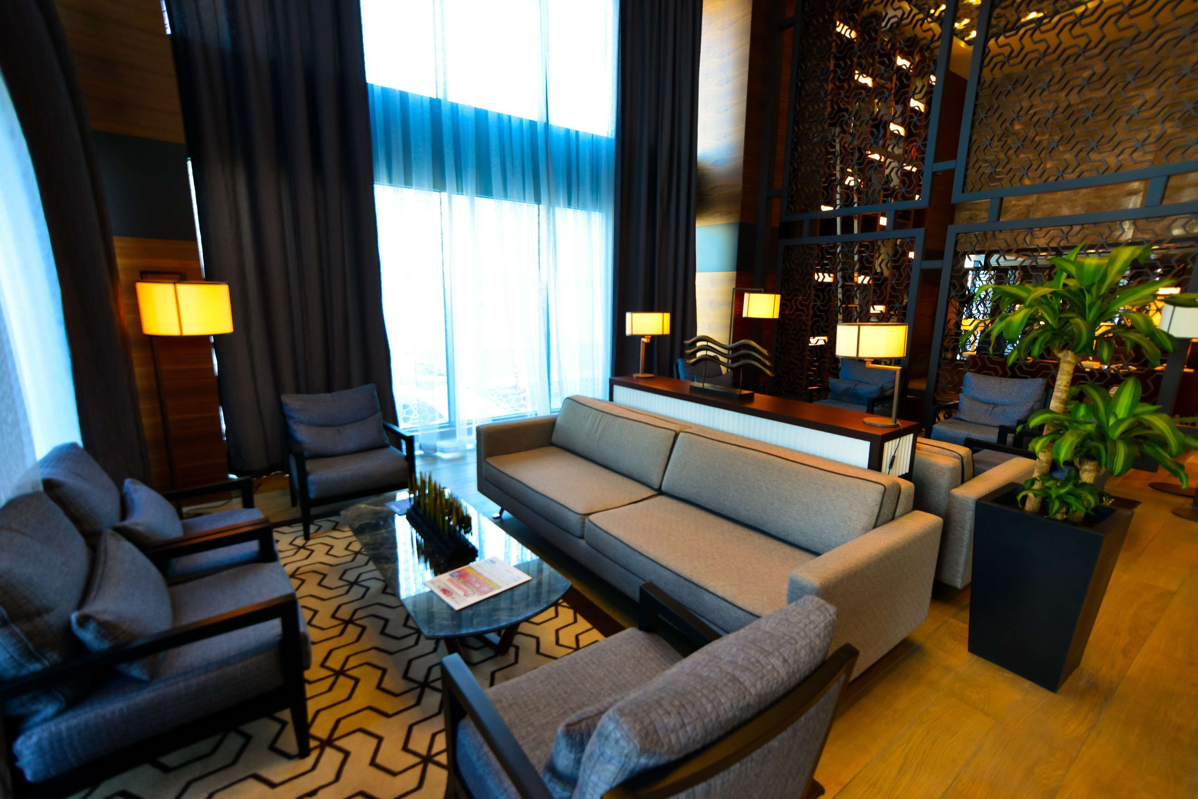 Um hall de hotel moderno com um sofá, poltronas, uma mesa de centro e uma planta em vaso.