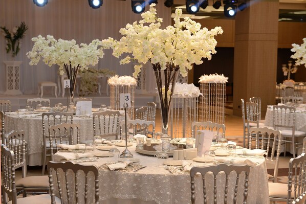A banquet hall with round tables set for a formal event, featuring white floral centerpieces and elegant table settings.