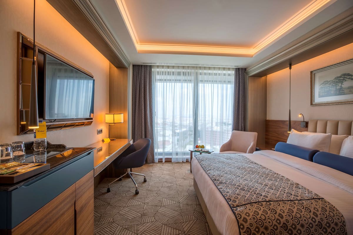 Une chambre d’hôtel avec un lit, un bureau, une chaise et une petite table sur laquelle se trouvent des fruits.