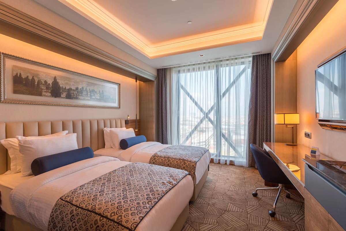 Une chambre d’hôtel avec deux lits, un bureau, une télévision et une grande fenêtre avec des rideaux.