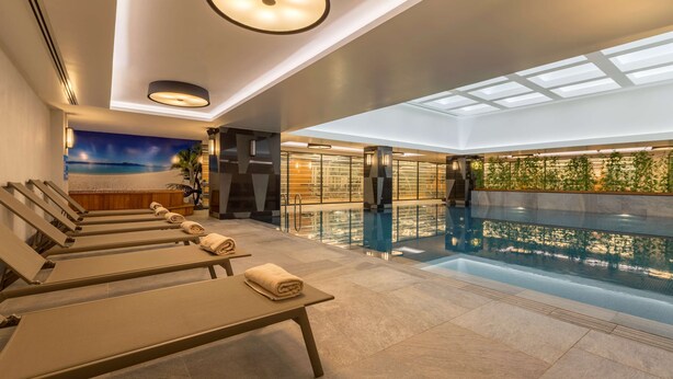 Un área de piscina interior moderna con sillones de descanso y una barrera de vidrio.