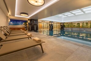 A modern indoor pool area with lounge chairs and a glass barrier.
