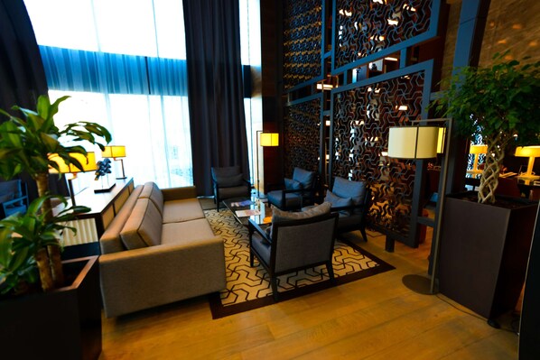 A modern hotel room with a sofa, chairs, a coffee table, and a decorative wall.