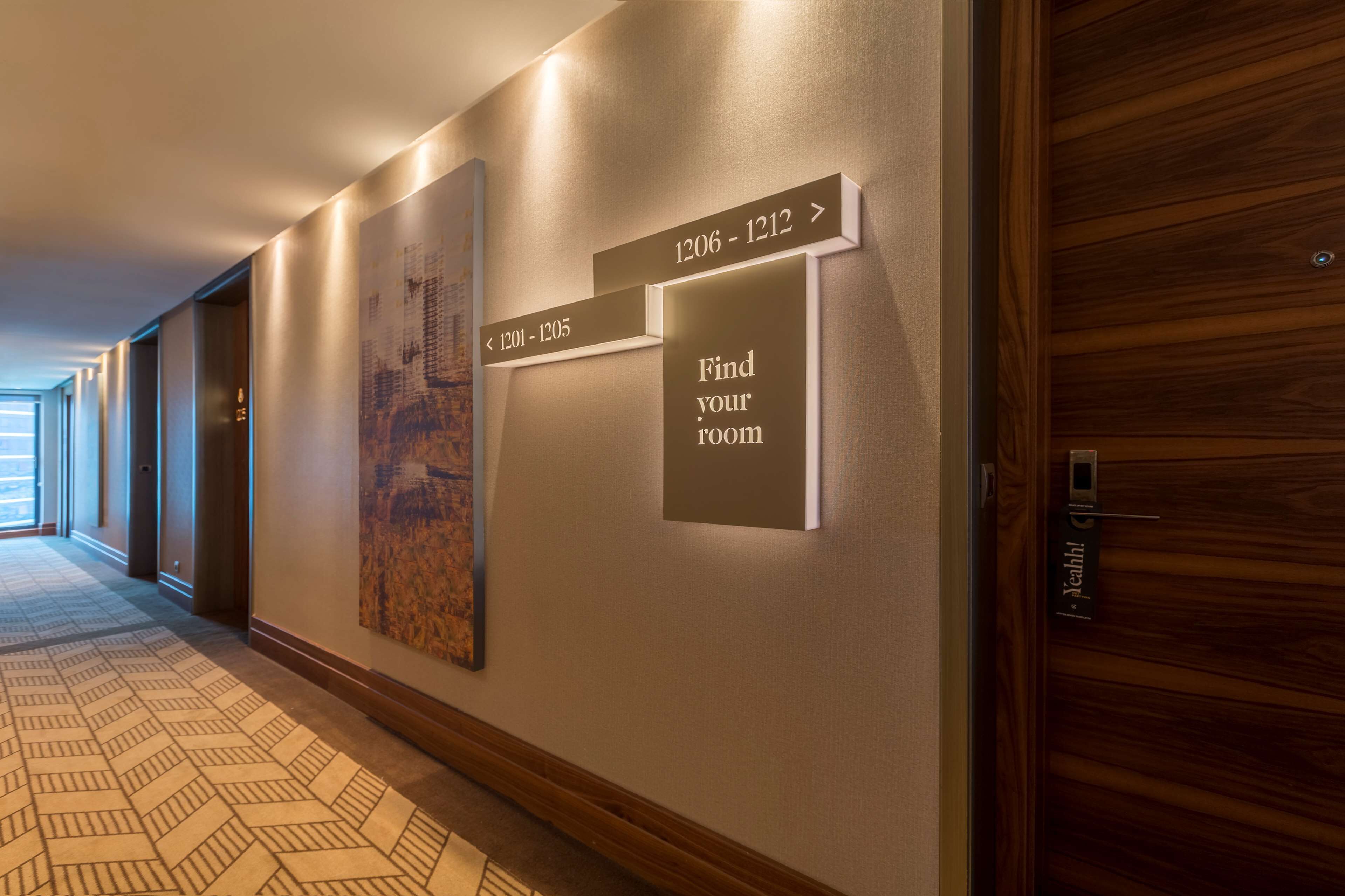 Un corridoio di hotel con cartelli direzionali che indicano i numeri delle camere e un cartello con la scritta 'Trova la tua camera'.