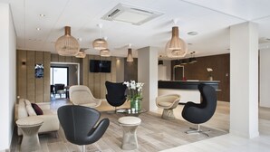 A modern hotel lobby with black and beige chairs, a glass coffee table, and wooden pendant lights. - Hôtel Valdys Thalasso & Spa - la Baie (Douarnenez)