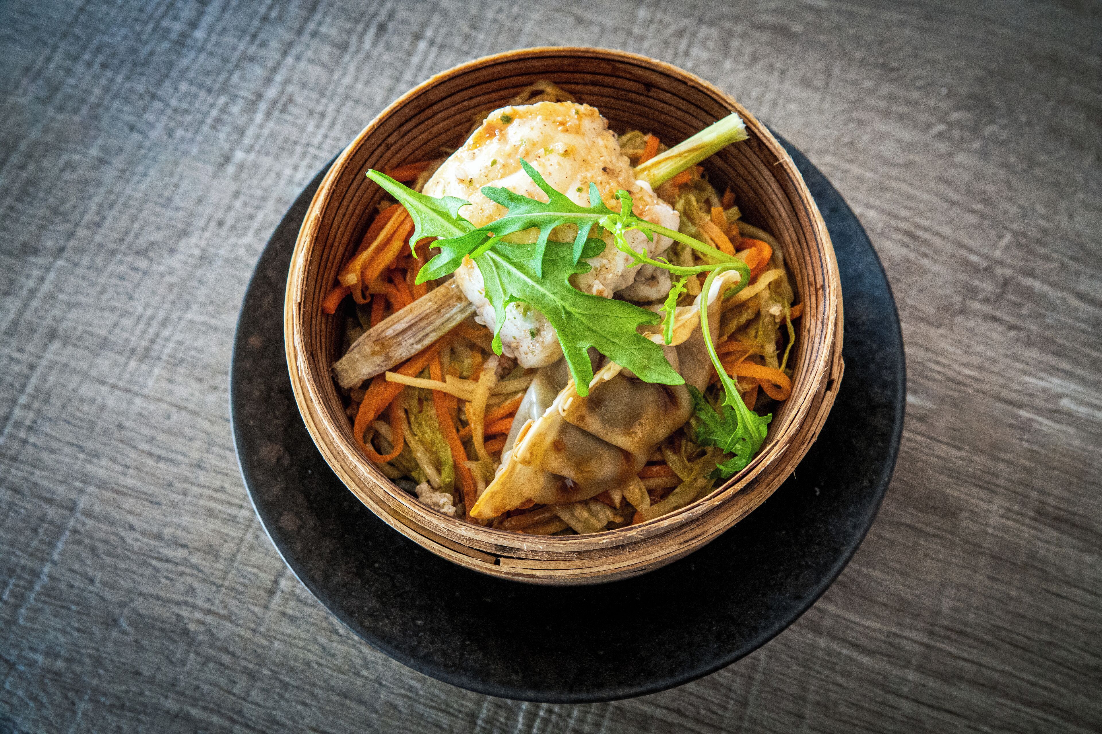 A bowl of food with vegetables and a piece of meat on a dark plate.