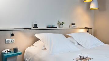 A neatly made bed with white linens, a bedside table with a lamp, a phone, and a cup.