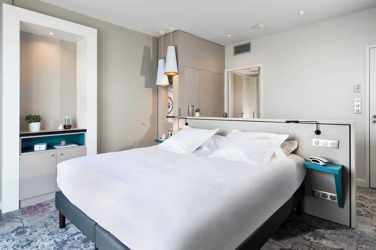 Ein modernes Hotelzimmer mit einem großen Bett, Nachttischen, einem Spiegel und einer eingebauten Ablage mit einer Pflanze.