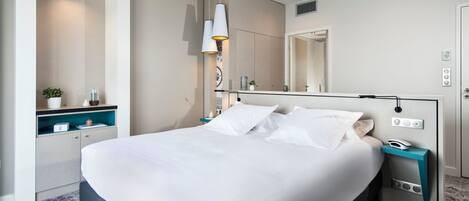 Ein modernes Hotelzimmer mit einem großen Bett, Nachttischen, einem Spiegel und einer eingebauten Ablage mit einer Pflanze.