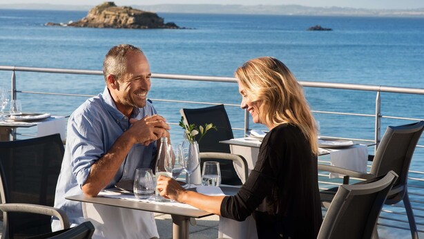 A couple dining at an outdoor table with a view of the sea and a rocky island in the distance. - Hôtel Valdys Thalasso & Spa - la Baie (Douarnenez)