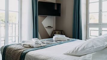 A hotel room with a bed, a flat-screen TV mounted on the wall, and a window with curtains.