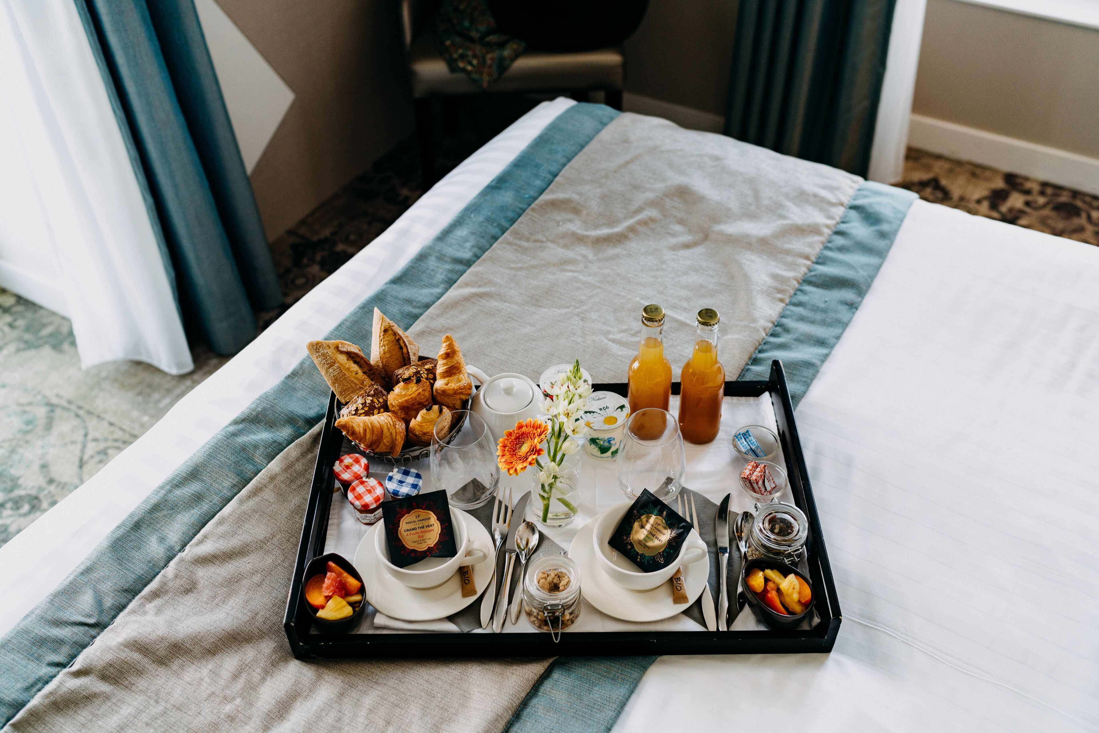 A breakfast tray with croissants, fruit, and beverages on a bed with a blue and white striped bedspread.