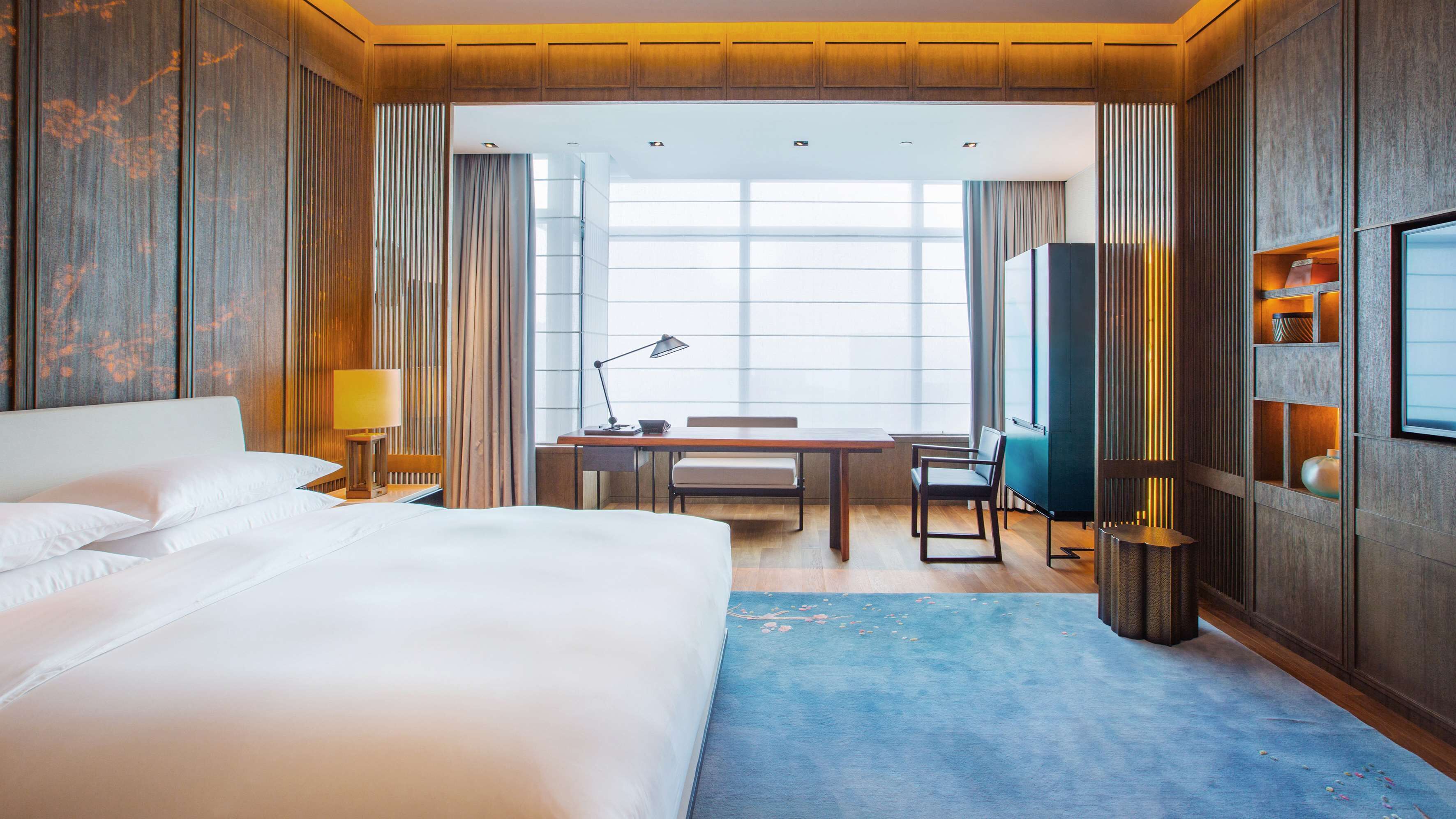 A hotel room with a large bed, a desk with a chair, a TV, and a window with curtains.