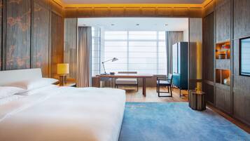 A hotel room with a large bed, a desk with a chair, a TV, and a window with curtains.