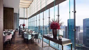 Restaurante moderno com teto alto e amplas janelas, oferecendo vista para a cidade.