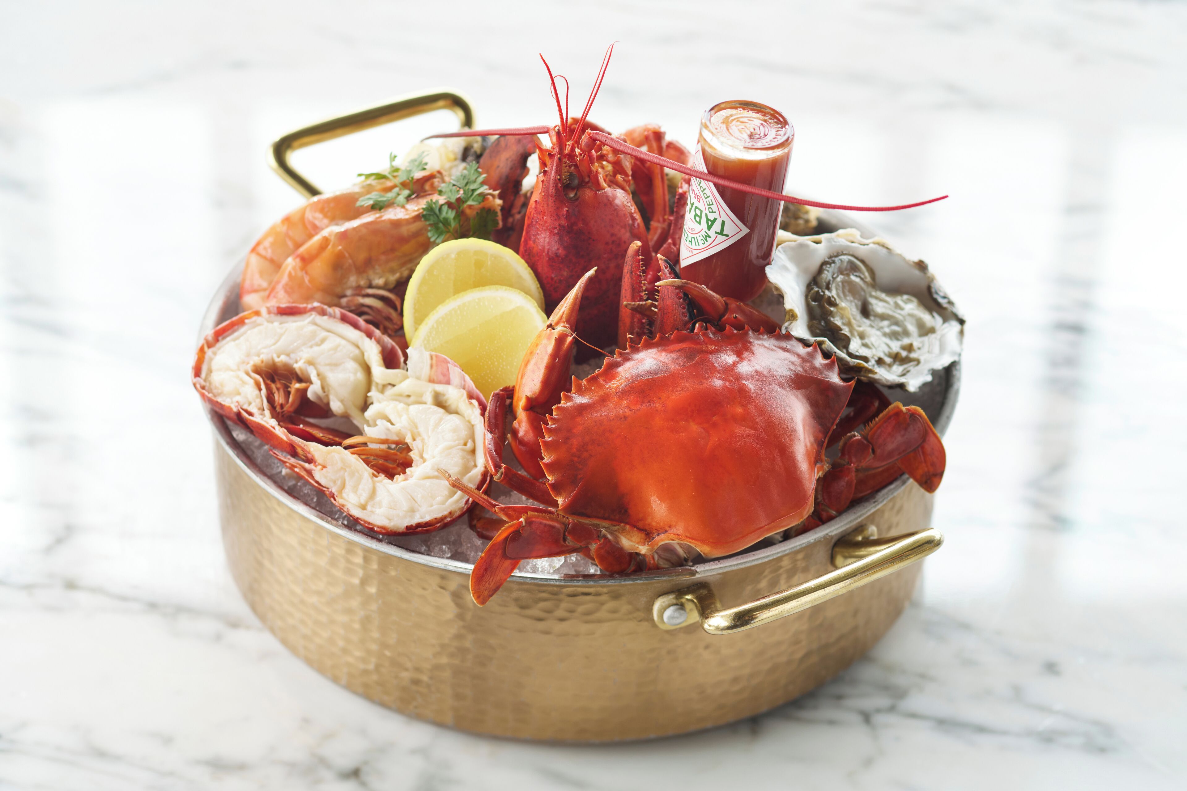 A seafood platter with lobster, oysters, lemon slices, and a bottle of sauce.