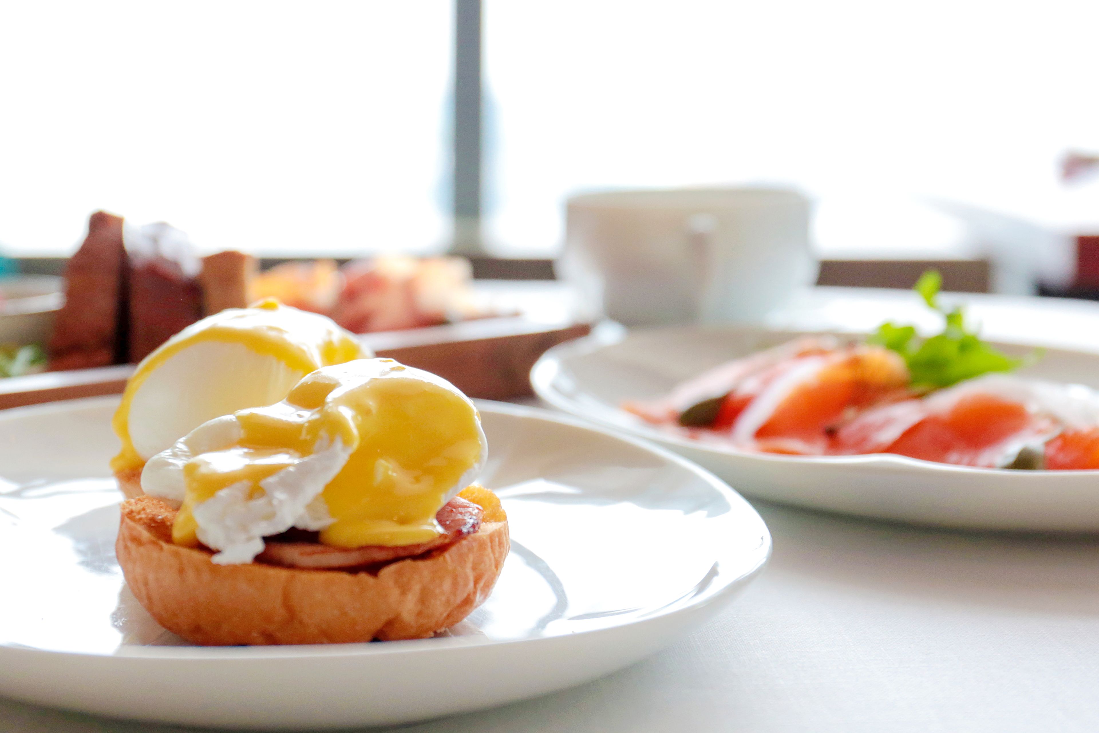 A breakfast setting with a plate of eggs Benedict and a plate of smoked salmon.