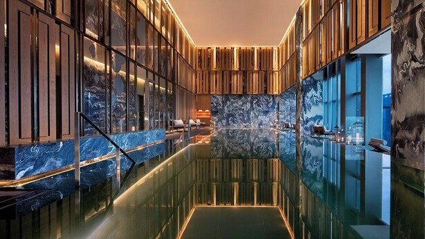 Um hall de hotel moderno com uma piscina refletora central, lambris de madeira e paredes de mármore.