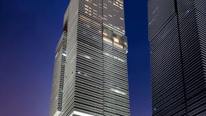 Dois edifícios altos com fachadas de vidro refletivas e céu azul.
